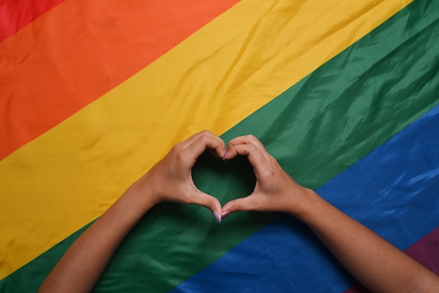 Le mani delle coppie lesbiche LGBT hanno preso la forma di un cuore sopra la bandiera LGBT arcobaleno Concetto di orgoglio LGBT