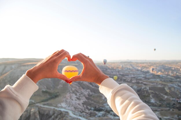 Le mani delle donne a forma di cuore sullo sfondo di palloncini volanti nel cielo della Cappadocia Vacanze in Turchia viaggiano durante una pandemia