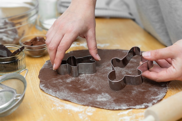 Le mani delle donne che cucinano i biscotti festivi del pan di zenzero di Natale. Cucinare biscotti o dessert al cioccolato.