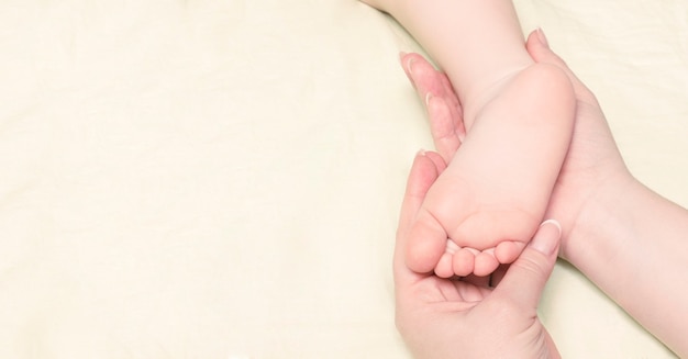 le mani delle donne che tengono il piede del bambino su uno sfondo di tessuto beige chiaro light
