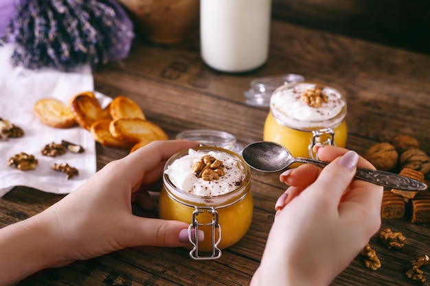 Le mani delle donne con il cucchiaio frullato di torta di zucca fatta in casa in barattolo di vetro con panna montata