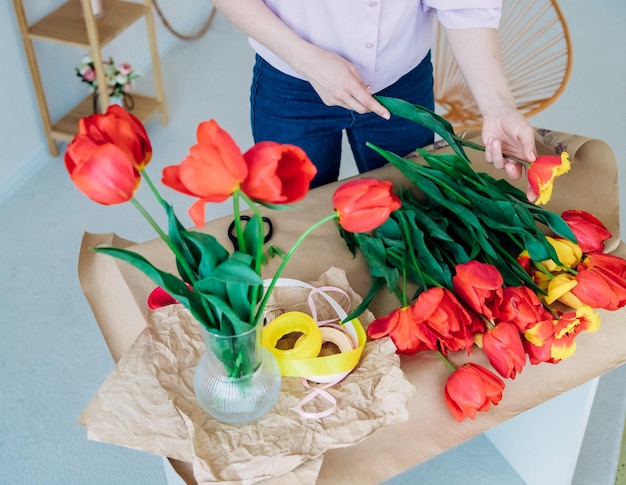 Le mani delle donne confezionano un bouquet festivo in carta da regalo Il fiorista fa un assemblaggio con tulipani rossi in officina Una donna al lavoro piccola impresa o hobby