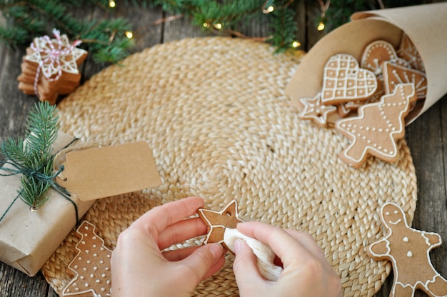 Le mani delle donne decorano i biscotti di pan di zenzero di Natale con glassa di zucchero sul bellissimo legno.