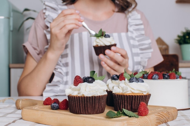 Le mani delle donne decorano i cupcake con la crema. Concetto di professione pasticcere.