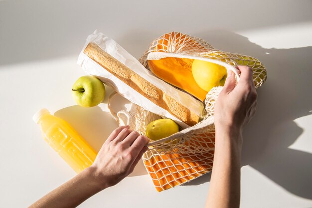 Le mani delle donne estraggono il cibo da una borsa della spesa su un tavolo bianco Vista dall'alto piatto