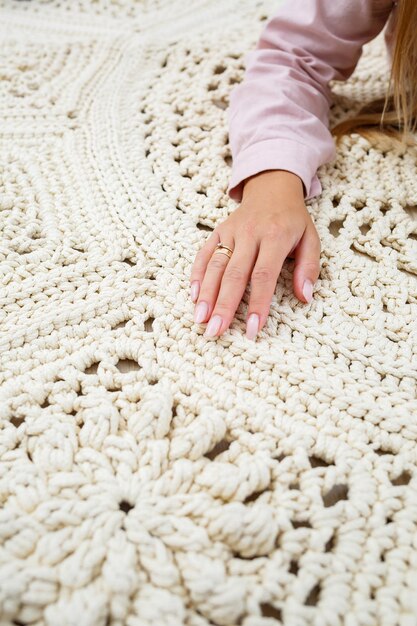 Le mani delle donne giacciono su un plaid di lana a maglia grezza su un pavimento in legno vista dall'alto Tappeto fatto a mano