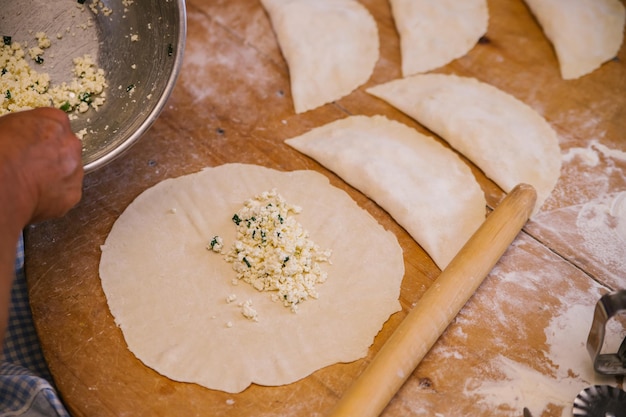 Le mani delle donne nel processo di cottura di kutaba o cheburek carne macinata e cipolle nell'impasto Ricotta e cipolla nell'impasto Cucina greca caucasica tartara azerbaigiana