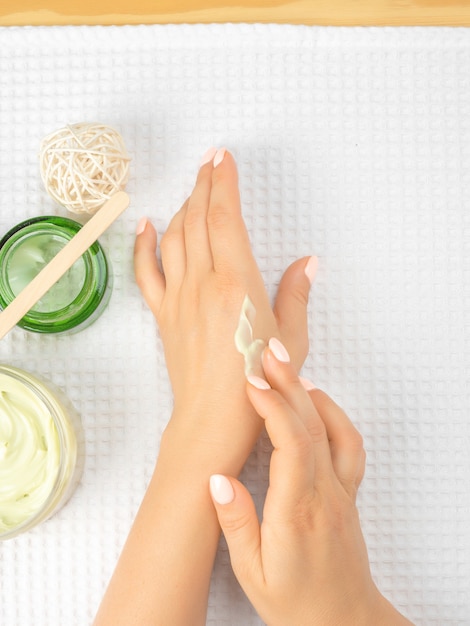 Le mani delle donne nel processo di diffusione della crema e un barattolo di crema naturale su asciugamani bianchi. Le mani fioriscono le donne dei cosmetici naturali, le mani della donna che applicano la crema idratante sulla pelle