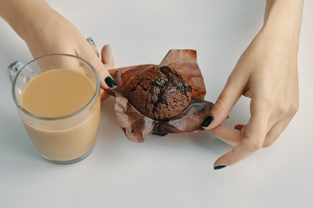 Le mani delle donne scartano il muffin al cioccolato tazza di caffè sul tavolo bianco mattina colazione romantica cacao e...