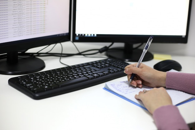 Le mani delle donne scrivono in un taccuino contro il monitor di un computer