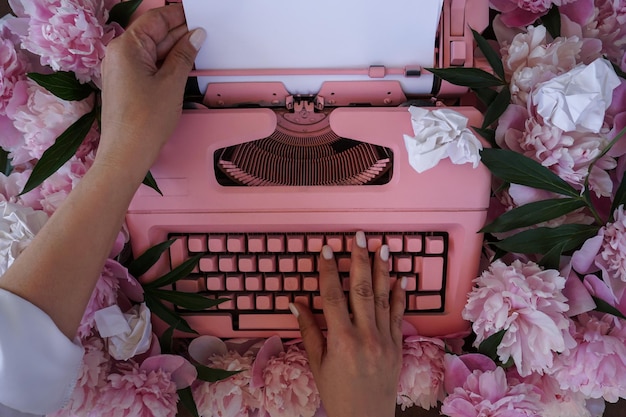 Le mani delle donne stanno digitando su una vecchia macchina da scrivere tra le peonie