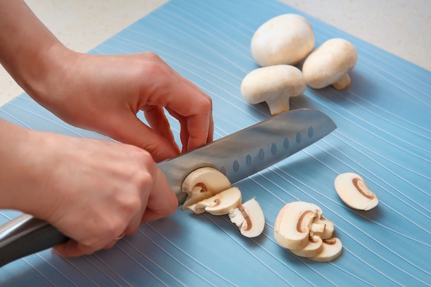 Le mani delle donne tagliano i funghi champignon a fette.