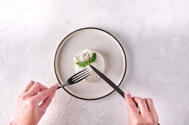 Le mani delle donne tagliate con coltello nero e forchetta burrata con basilico su piastra leggera vista dall'alto copia