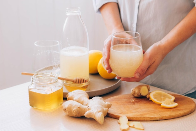 Le mani delle donne tengono il bicchiere con una bevanda a base di radice di zenzero miele limone antiossidante appena preparato