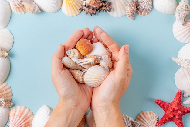 Le mani delle donne tengono le conchiglie su un fondo blu dell'estate con differenti conchiglie e stelle marine