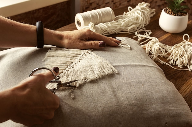 Le mani delle donne tessono il macramè in un laboratorio domestico. Stile di vita bohémien. Concetto di hobby, messa a fuoco selettiva