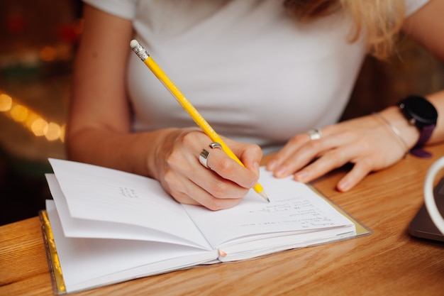 Le mani delle ragazze scrivono a matita gialla su una pagina bianca del blocco note