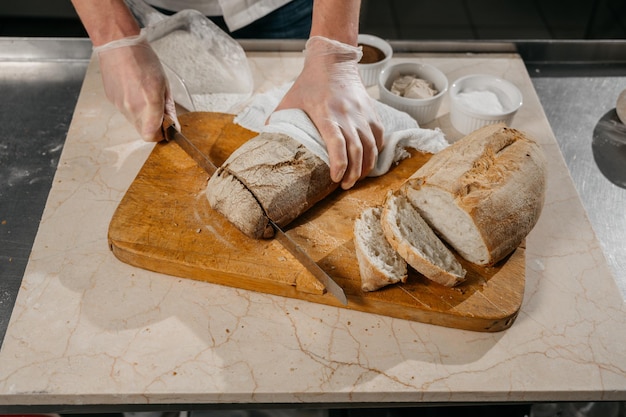 Le mani dello chef maschio tagliano il pane. Foto di alta qualità