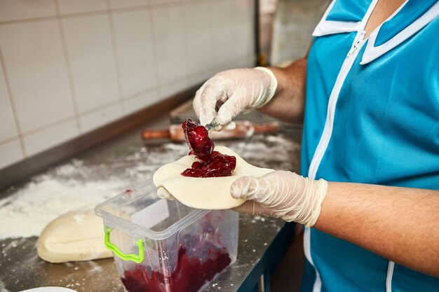 Le mani dello chef preparano torte di ciliegie nella cucina del ristorante. Il processo di preparazione dei panini dolci. Pasta cruda per la cottura in forno.