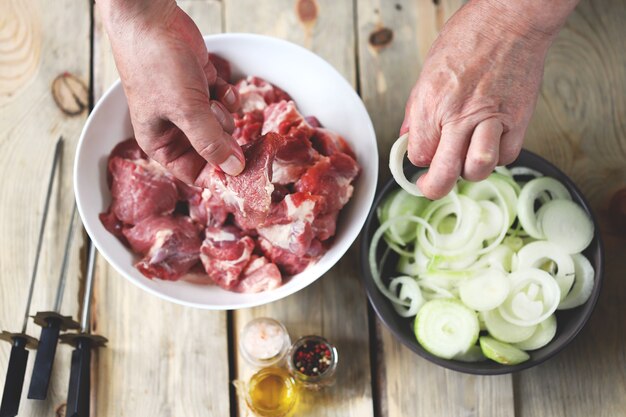 Le mani dello chef stanno preparando kebab di carne con cipolle. Una ciotola di carne cruda e una ciotola di cipolle. Cucina barbecue.