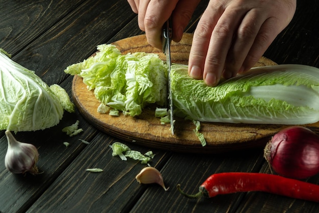 Le mani dello chef stanno tagliando foglie di lattuga fresca su un tagliere per insalata di vitamine