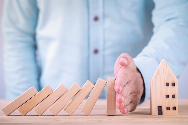 Le mani di affari fermano i blocchi di legno dell'effetto domino prima di distruggere la casa, finanziamento della protezione della proprietà privata dal concetto di effetto domino