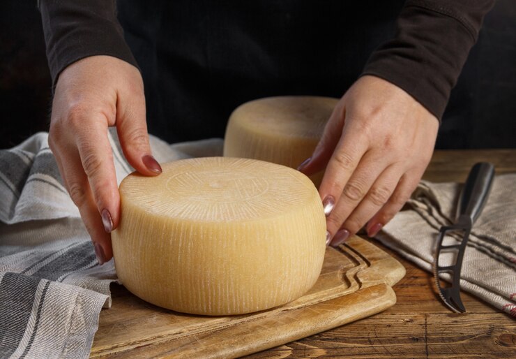 Foto le mani di qualcuno mettono una ruota di formaggio fresco fatto in casa su una tavola di legno da vicino