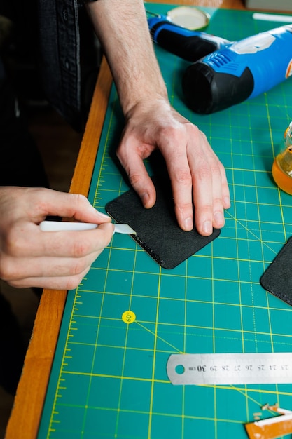 Le mani di un artigiano professionista fanno un portafoglio in pelle nuovo, pulito, in vera pelle, primo piano ritagliato