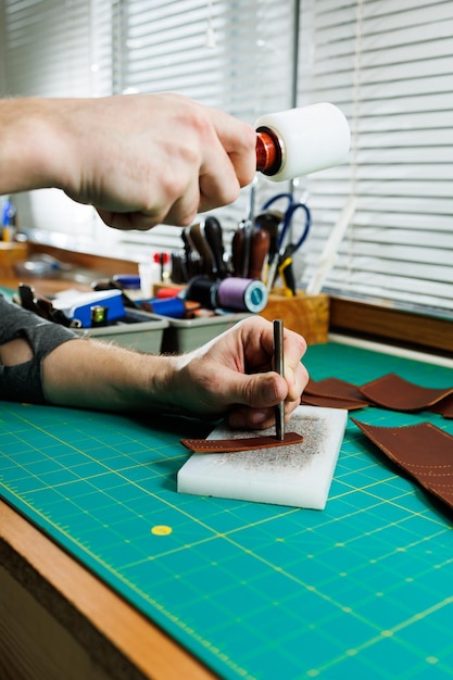 Le mani di un artigiano professionista fanno un portafoglio in pelle nuovo, pulito, in vera pelle, primo piano ritagliato