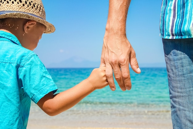 Le mani di un genitore e di un figlio felici in riva al mare nel viaggio nella natura