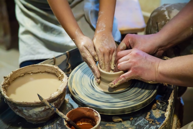 Le mani di un maestro e di uno studente fanno una brocca su una ruota da vasaio di argilla gialla. Messa a fuoco selettiva sulle mani