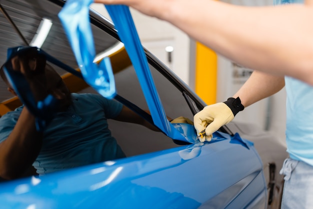 Le mani di un meccanico maschio installano una pellicola o un foglio di vinile protettivo sulla portiera del veicolo. Il lavoratore fa i dettagli automatici. Protezione della vernice dell'auto, messa a punto professionale