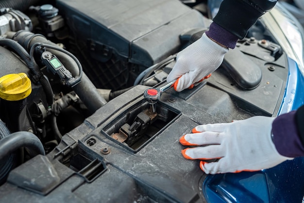 Le mani di un meccanico uomo forte in guanti riparano l'auto sotto il cofano