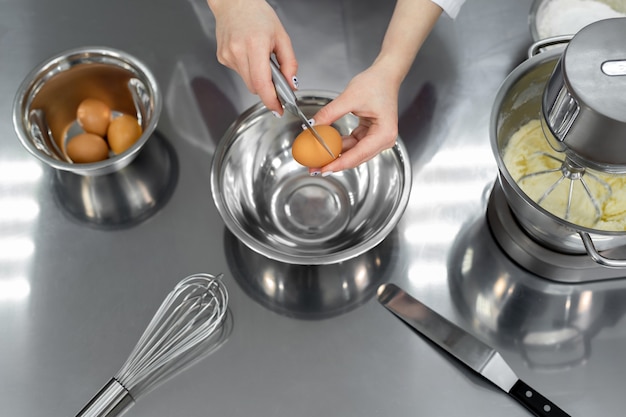 Le mani di un pasticcere rompono un uovo con un coltello in una cucina professionale.