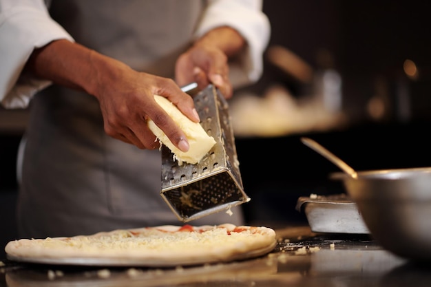 Le mani di un pizzaiolo che tritta la testa di formaggio mozzarella su una piccola pizza