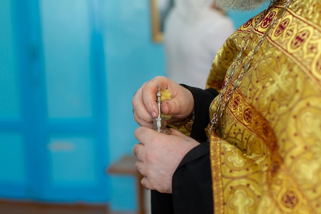 Le mani di un prete ortodosso tengono una bottiglia di olio di mirra per il rito del battesimo