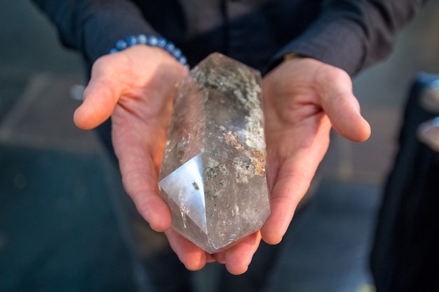 Le mani di un uomo che regge un cristallo di quarzo grande e leggero sembrano potenti.