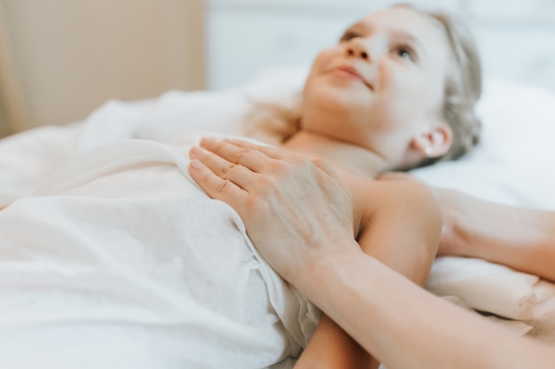 Le mani di un vero dottore osteopata fanno terapia fisiologica ed emotiva per una bambina di otto anni. sessione di trattamento di osteopatia pediatrica. medicina alternativa. prendersi cura della salute del bambino