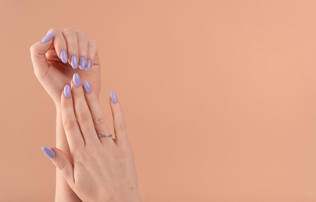 Le mani di una bella lavanda viola per unghie ben curate smalto gel su uno sfondo beige