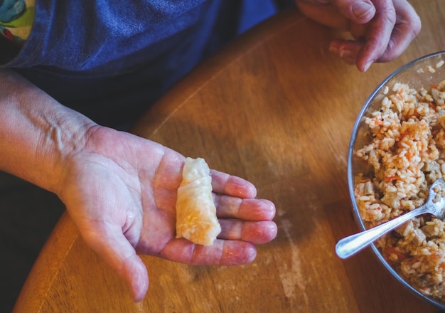 Le mani di una donna anziana indicano un cavolo ripieno di crauti crudi ripieni di riso e carne