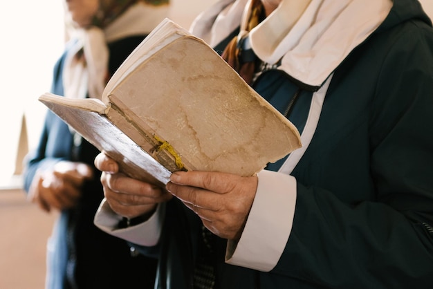 Le mani di una donna anziana reggono un vecchio libro di preghiere in chiesa