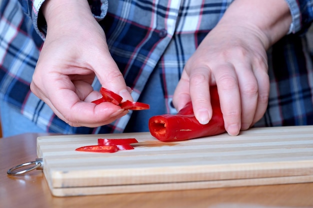 Le mani di una donna anziana tagliano i peperoni rossi e li espongono in cucina su un tavolo marrone senza un primo piano del viso