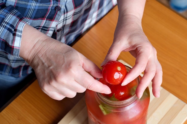 Le mani di una donna anziana tirano fuori deliziosi pomodori marinati fatti in casa da un barattolo in cucina su un tavolo marrone senza un primo piano del viso