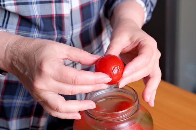 Le mani di una donna anziana tirano fuori deliziosi pomodori marinati fatti in casa da un barattolo in cucina su un tavolo marrone senza un primo piano del viso