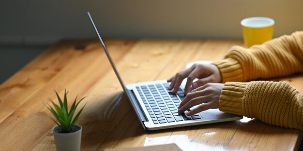 Le mani di una donna che usa un portatile bianco sullo schermo vuoto alla scrivania di legno