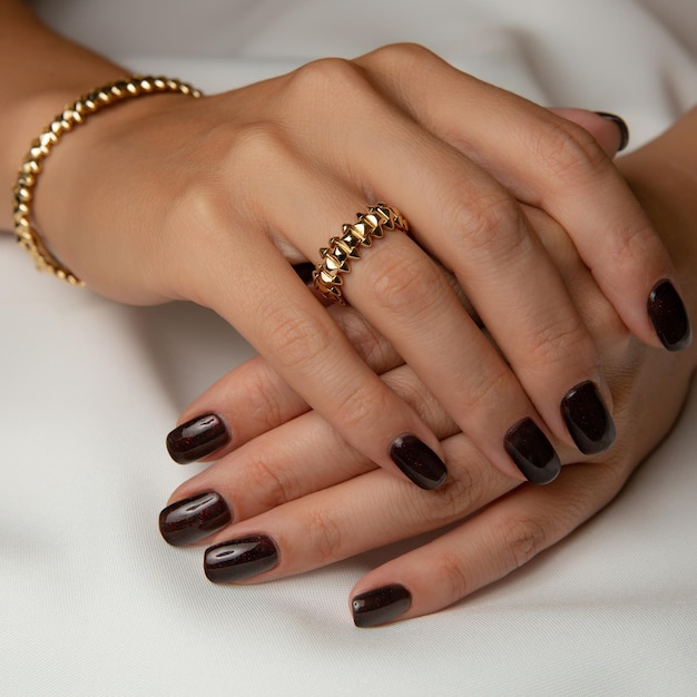 Le mani di una donna con un braccialetto d'oro e uno smalto nero.