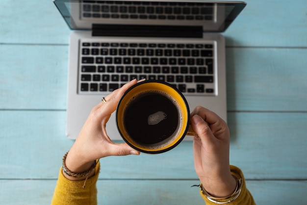 Le mani di una donna con una tazza di caffè hanno lavorato sul suo laptop. Concetto di lavoro a casa.