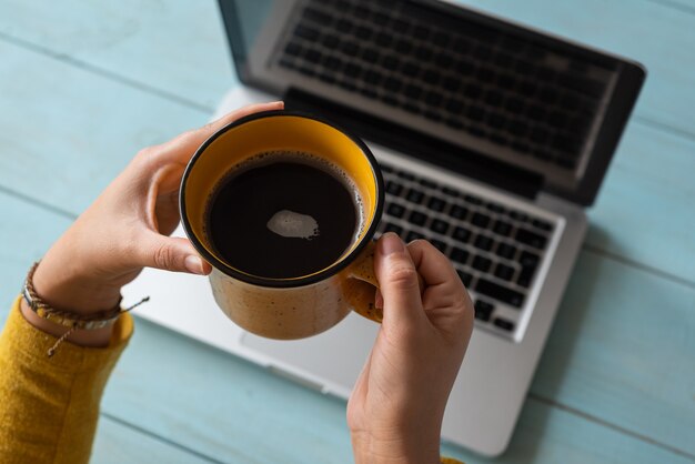 Le mani di una donna con una tazza di caffè hanno lavorato sul suo laptop. Concetto di lavoro a casa.