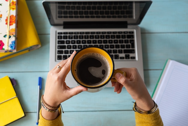 Le mani di una donna con una tazza di caffè hanno lavorato sul suo laptop. Concetto di lavoro a casa.