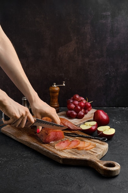 Le mani di una donna hanno tagliato una fetta di prosciutto di tacchino essiccato all'aria sul tagliere di legno